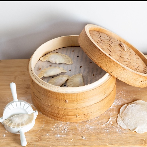 The steamer is lined with steamer paper, and on top of it are the freshly wrapped dumplings.