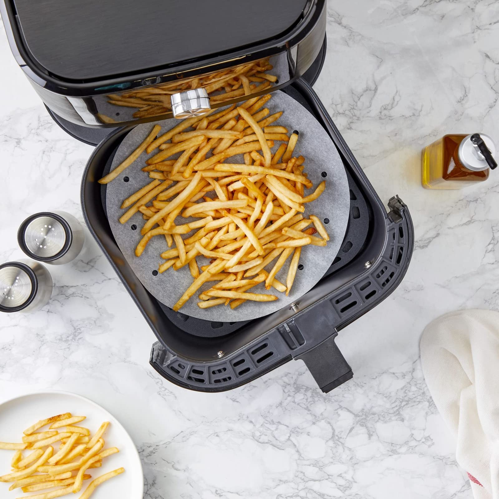 French fries in an air fryer basket lined with round air fryer paper with holes
