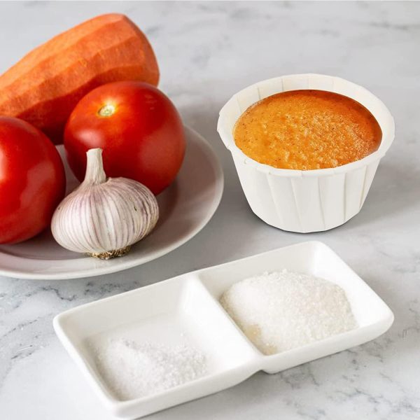 white paper sauce cup with thick orange sauce beside fresh tomatoes, garlic, and carrot